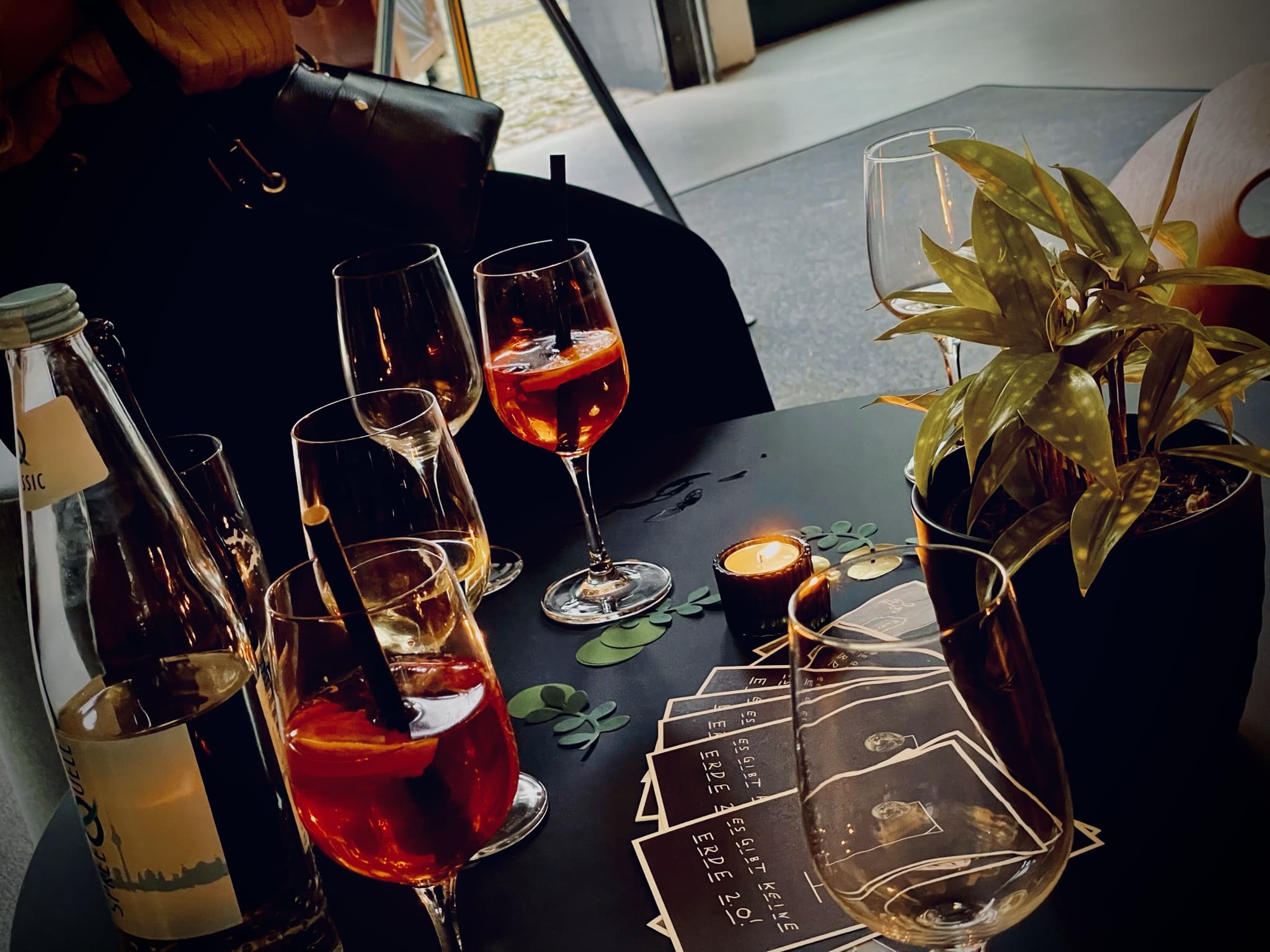 A section of a black table on which there are various drinks for toasting and postcards with the inscription "There is no Earth 2.0!"