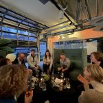 Mehrere Personen (das Team des Grüner Strom Label e.V.) sitzen um einen Tisch mit Gläsern und Snacks zusammen und lachen