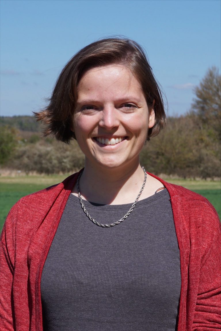 Photo of Katharina Wawer, a woman with shorter brown hair in a red cardigan, smiling at the camera